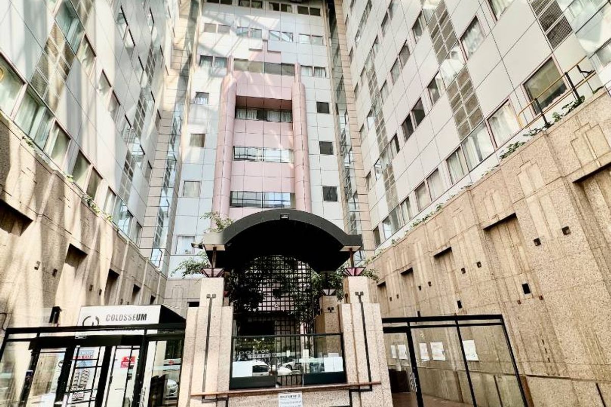 A large, modern atrium courtyard featuring a glass roof, stone-clad walls, and secure glass entrance doors within a multi-story building complex.