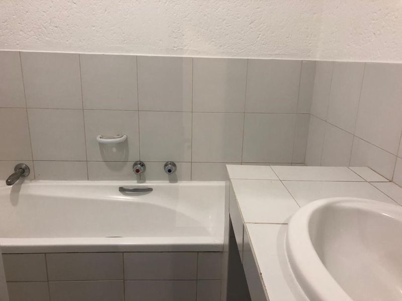 A functional bathroom featuring a built-in bathtub and a tiled vanity with an integrated sink, finished with neutral wall tiling.