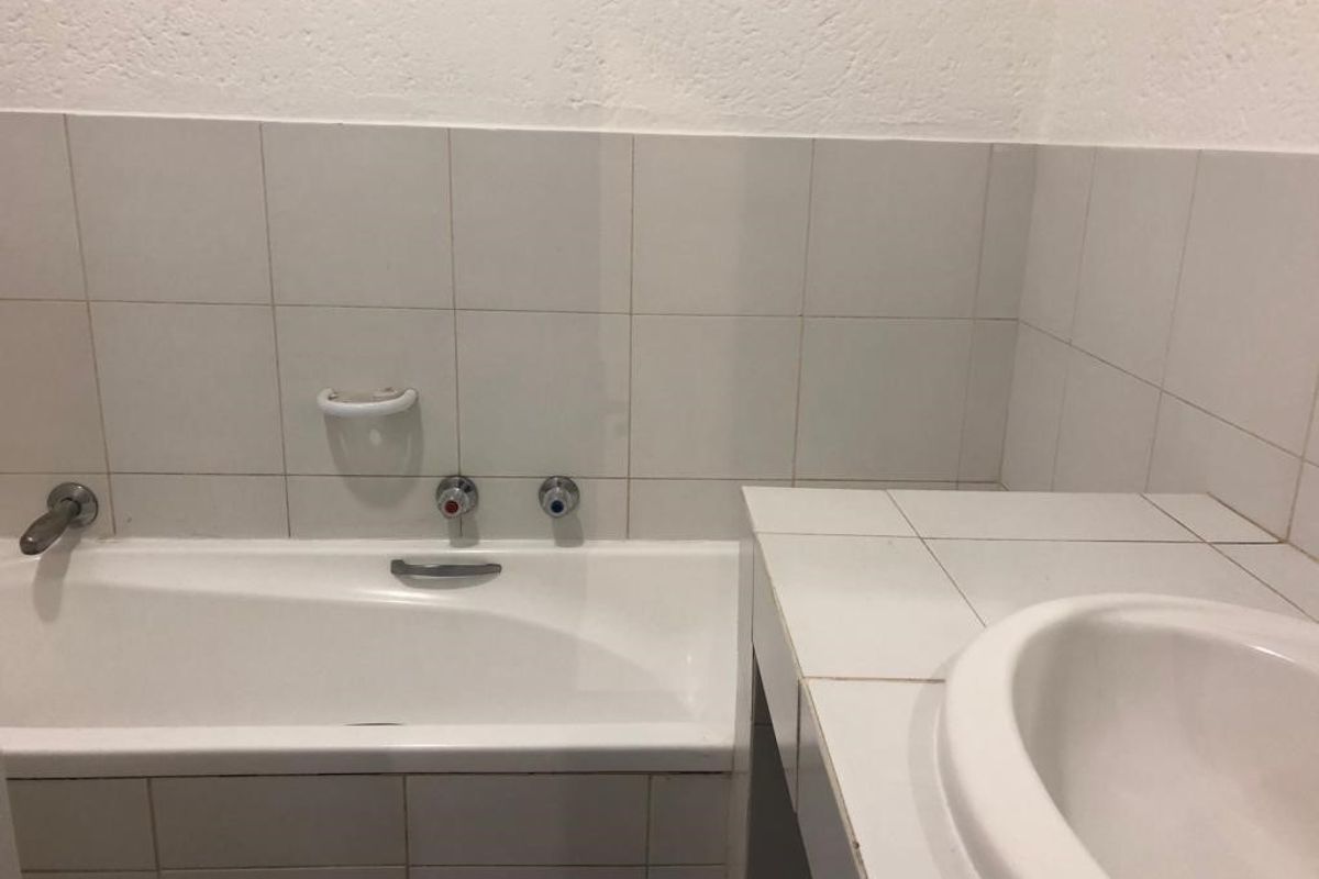 A functional bathroom featuring a built-in bathtub and a tiled vanity with an integrated sink, finished with neutral wall tiling.