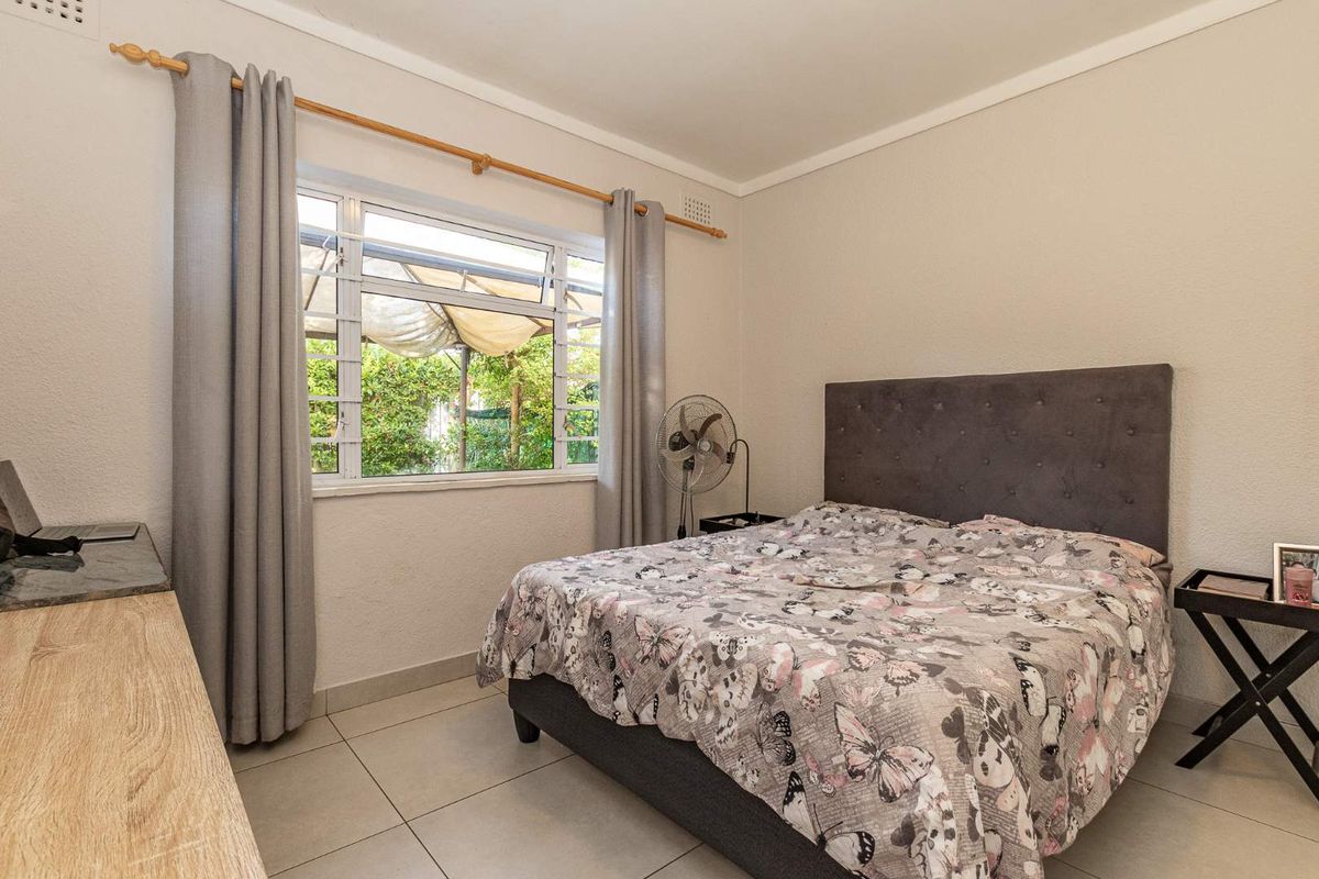 A well-lit bedroom featuring neutral tiled flooring, a large window with curtain rod, and a clean, functional layout.