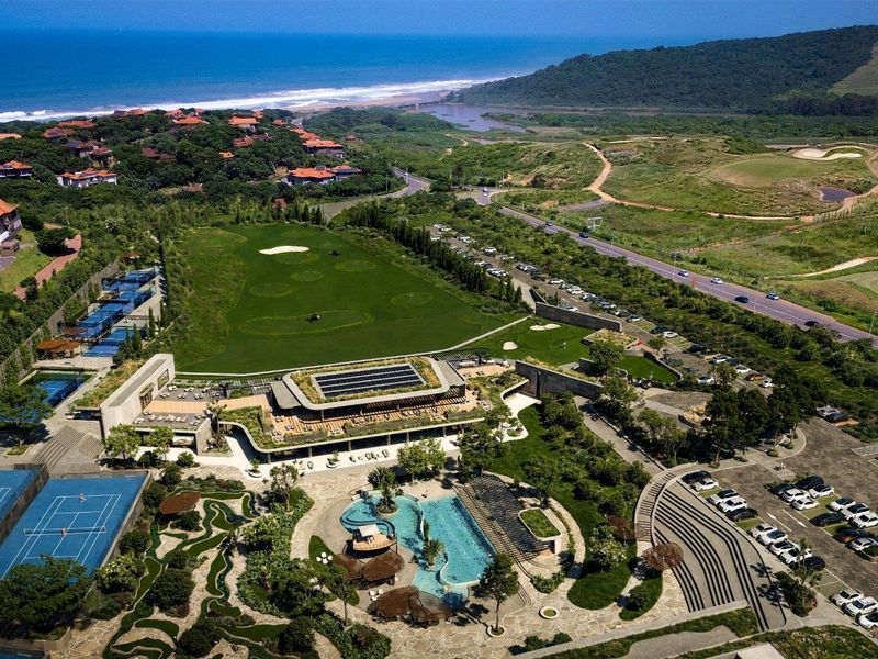 Aerial view of a luxury estate featuring a swimming pool, tennis courts, golf course, and extensive landscaped grounds with coastal views.
