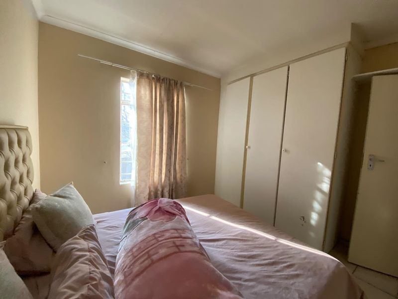 A functional bedroom featuring built-in cupboards and a window with security bars, offering a practical layout for a townhouse setting.
