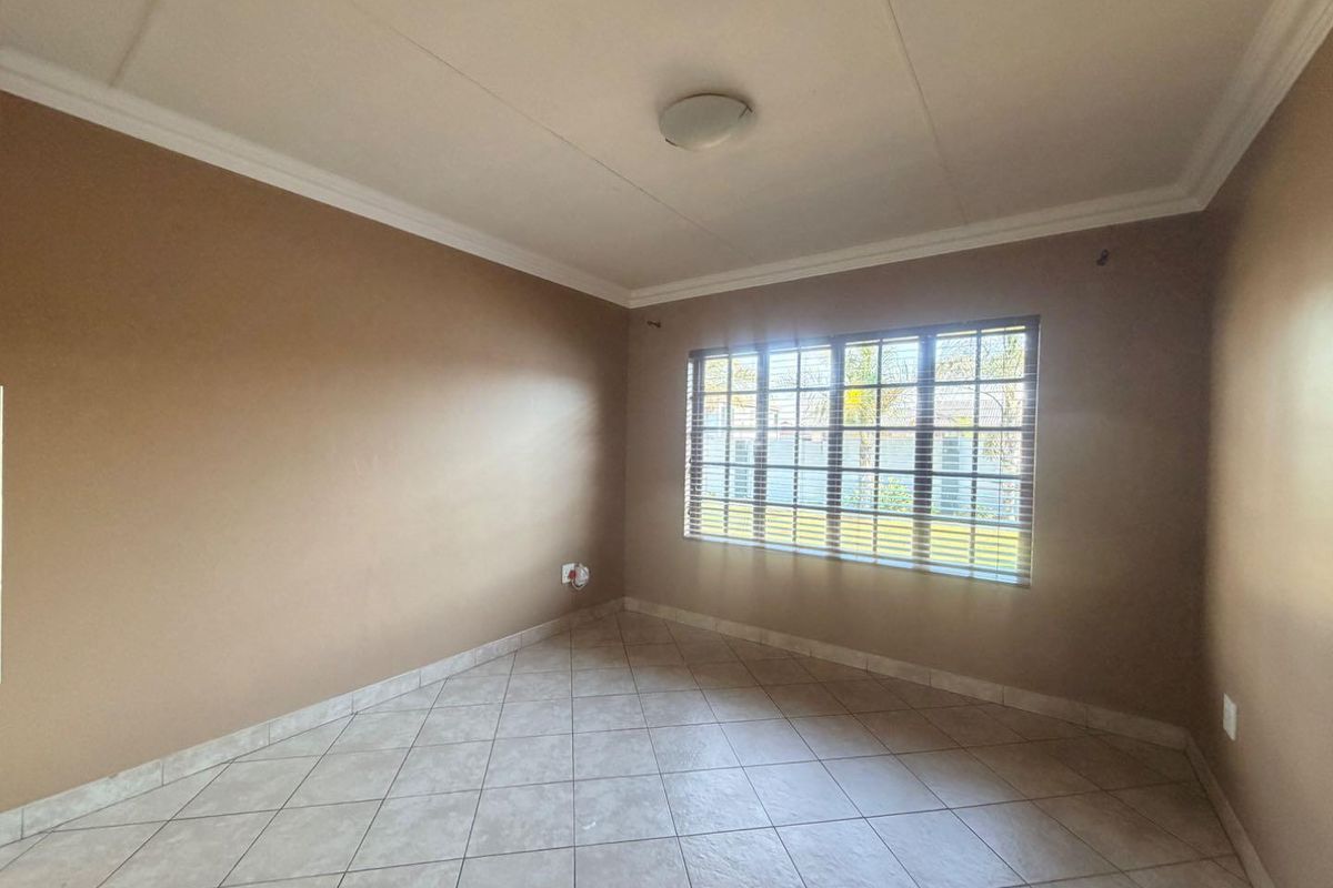 A clean, empty bedroom featuring neutral-toned walls, tiled flooring, and a window fitted with horizontal blinds.