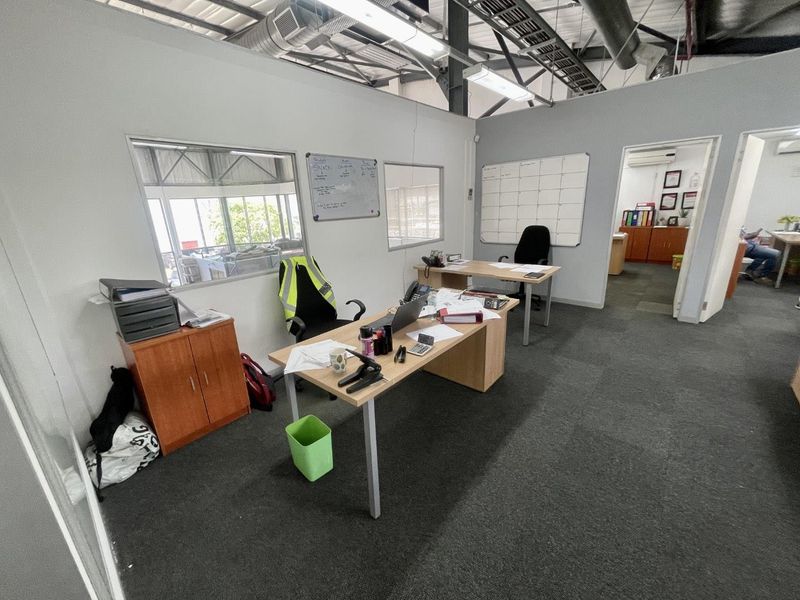 A functional office space featuring exposed industrial ceilings, carpeted flooring, and internal glass partitions, providing a practical work environment.