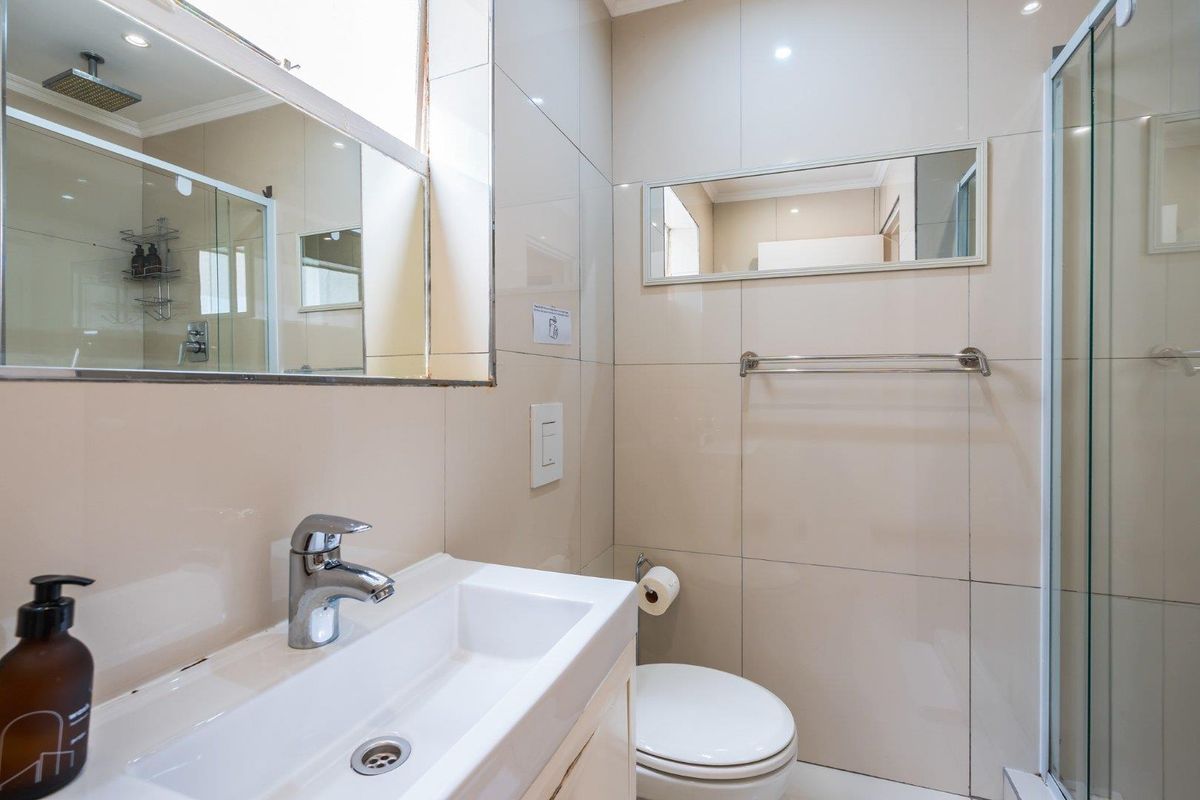Modern bathroom featuring a vanity basin, wall-mounted mirror, toilet, and a glass-enclosed shower with tiled walls.