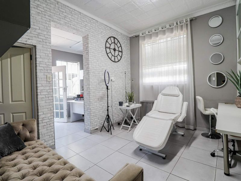 A functional office space featuring tiled flooring, faux brick accent wall, and a large window providing natural light, suitable for professional or clinical use.