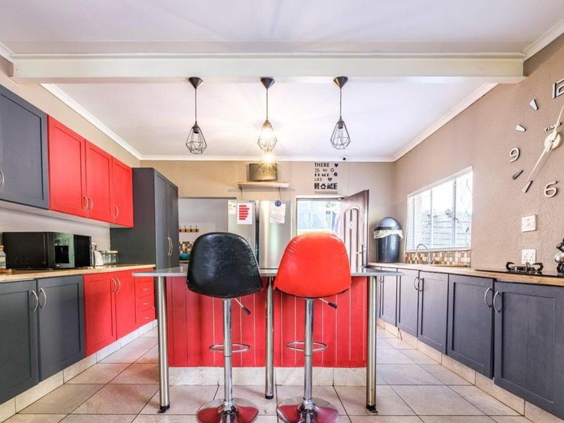 A functional kitchen featuring a central island, contrasting red and dark grey cabinetry, tiled flooring, and modern pendant lighting.