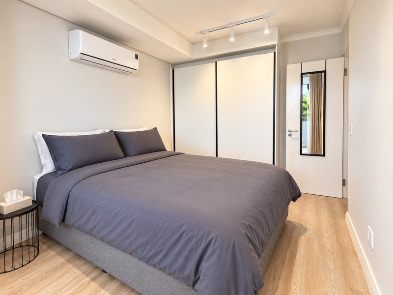 Modern bedroom featuring light laminate flooring, built-in wardrobe, split-system air conditioning, and track lighting for a clean, contemporary aesthetic.