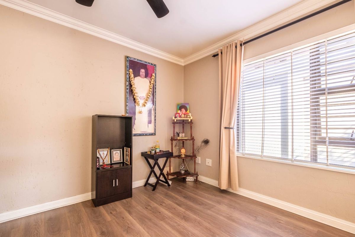 A well-maintained bedroom featuring laminate flooring, crown molding, and a ceiling fan, with natural light provided by a large window with venetian blinds.