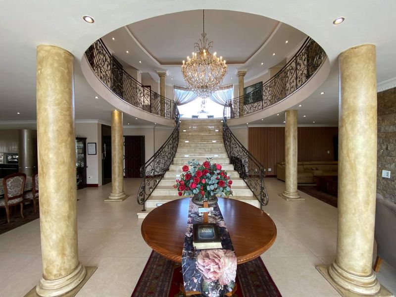 Grand entrance hall featuring a sweeping staircase with ornate wrought iron balustrades, decorative columns, and a central chandelier.