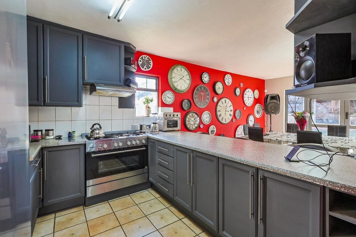 A functional kitchen featuring dark grey cabinetry, gas stove with extractor fan, laminate countertops, and tiled flooring, offering a practical layout for daily cooking.