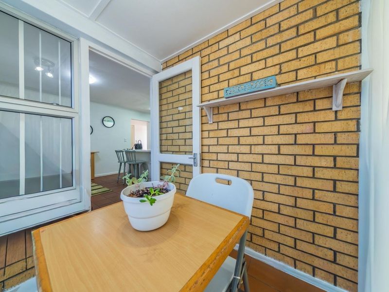 A covered patio area featuring an exposed brick wall, tiled flooring, and a fixed wall shelf, providing a cozy transition space to the interior.