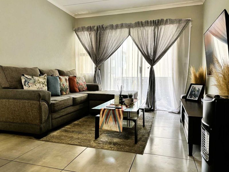 A well-maintained living room featuring large format floor tiles, coved ceilings, and a sliding glass door providing access to an outdoor area.
