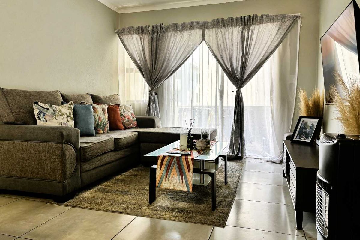 A well-maintained living room featuring large format floor tiles, coved ceilings, and a sliding glass door providing access to an outdoor area.