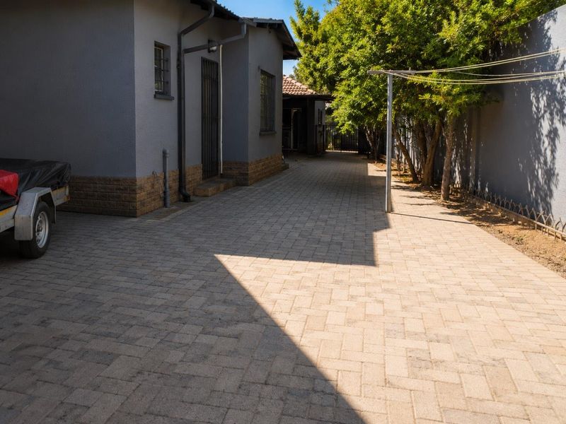 A paved side driveway and rear exterior area featuring a grey rendered facade with brick detailing and secure window bars.