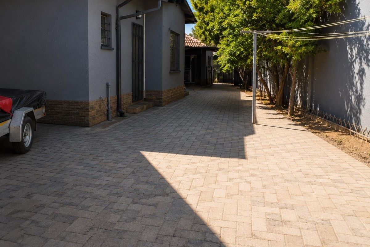 A paved side driveway and rear exterior area featuring a grey rendered facade with brick detailing and secure window bars.