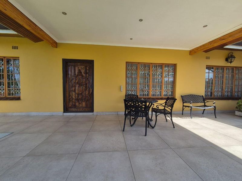 A spacious covered patio featuring large format floor tiles, timber ceiling beams, recessed lighting, and secure timber-framed windows.