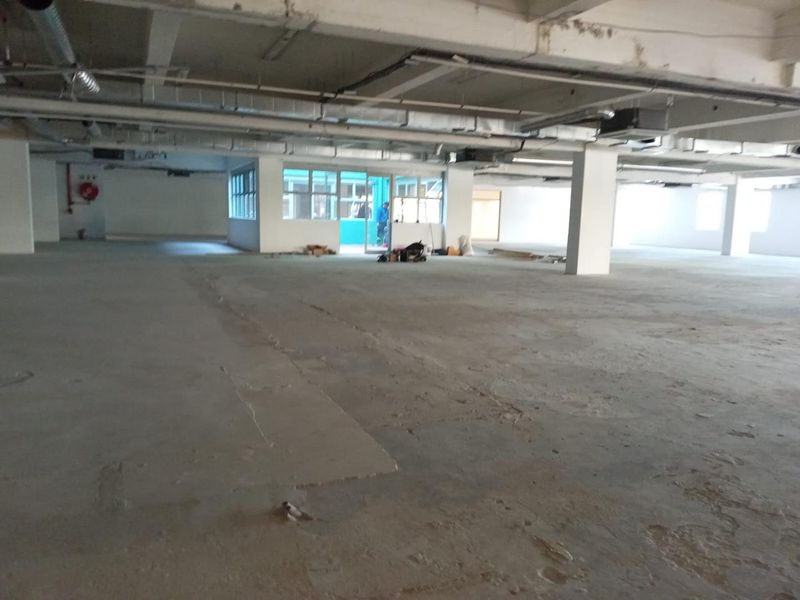 A large, open-plan commercial space featuring exposed concrete ceilings, industrial ductwork, and structural columns, currently in a shell condition.