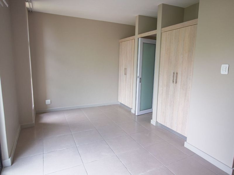 A bright, empty bedroom featuring neutral tiled flooring and modern built-in cupboards with a frosted glass door.
