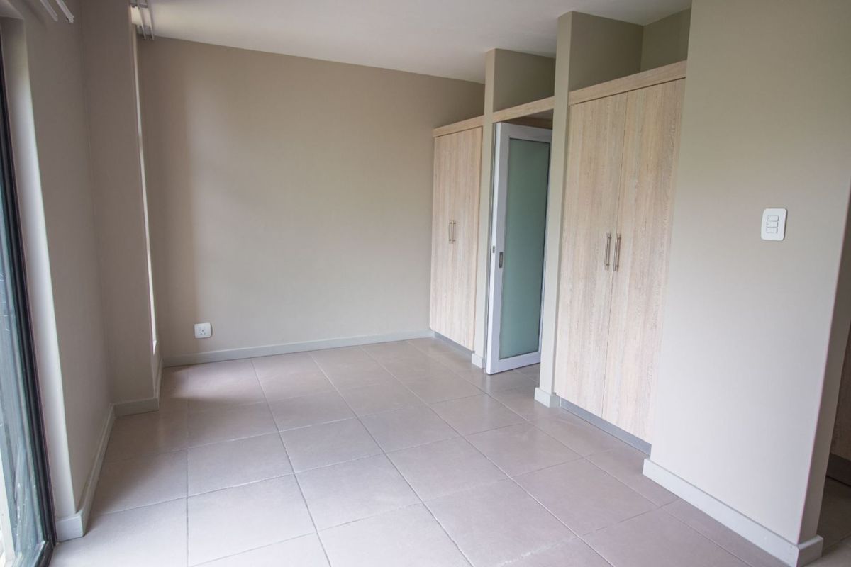 A bright, empty bedroom featuring neutral tiled flooring and modern built-in cupboards with a frosted glass door.