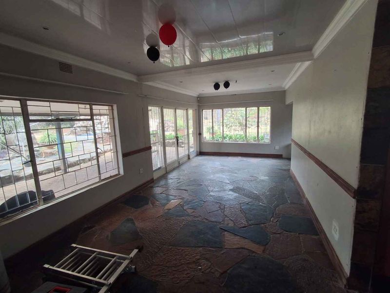 Spacious living area featuring natural slate tile flooring, a glossy ceiling finish, and large windows providing ample natural light and garden views.