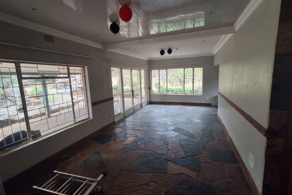 Spacious living area featuring natural slate tile flooring, a glossy ceiling finish, and large windows providing ample natural light and garden views.