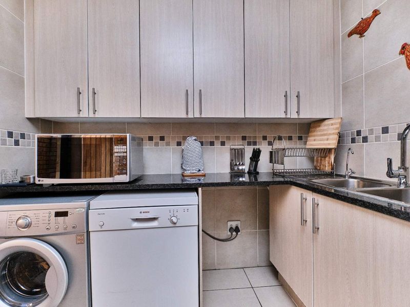 Functional scullery featuring light wood-finish cabinetry, granite countertops, a stainless steel double sink, and tiled backsplash with integrated appliance space.