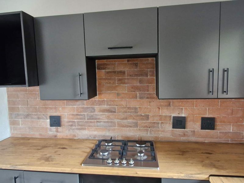 Modern kitchen featuring dark grey cabinetry, a timber-look countertop, and a stylish exposed brick splashback with an integrated gas hob.