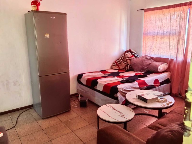 A bedroom featuring tiled flooring and a window with a curtain rod, currently used as a multi-purpose living space.