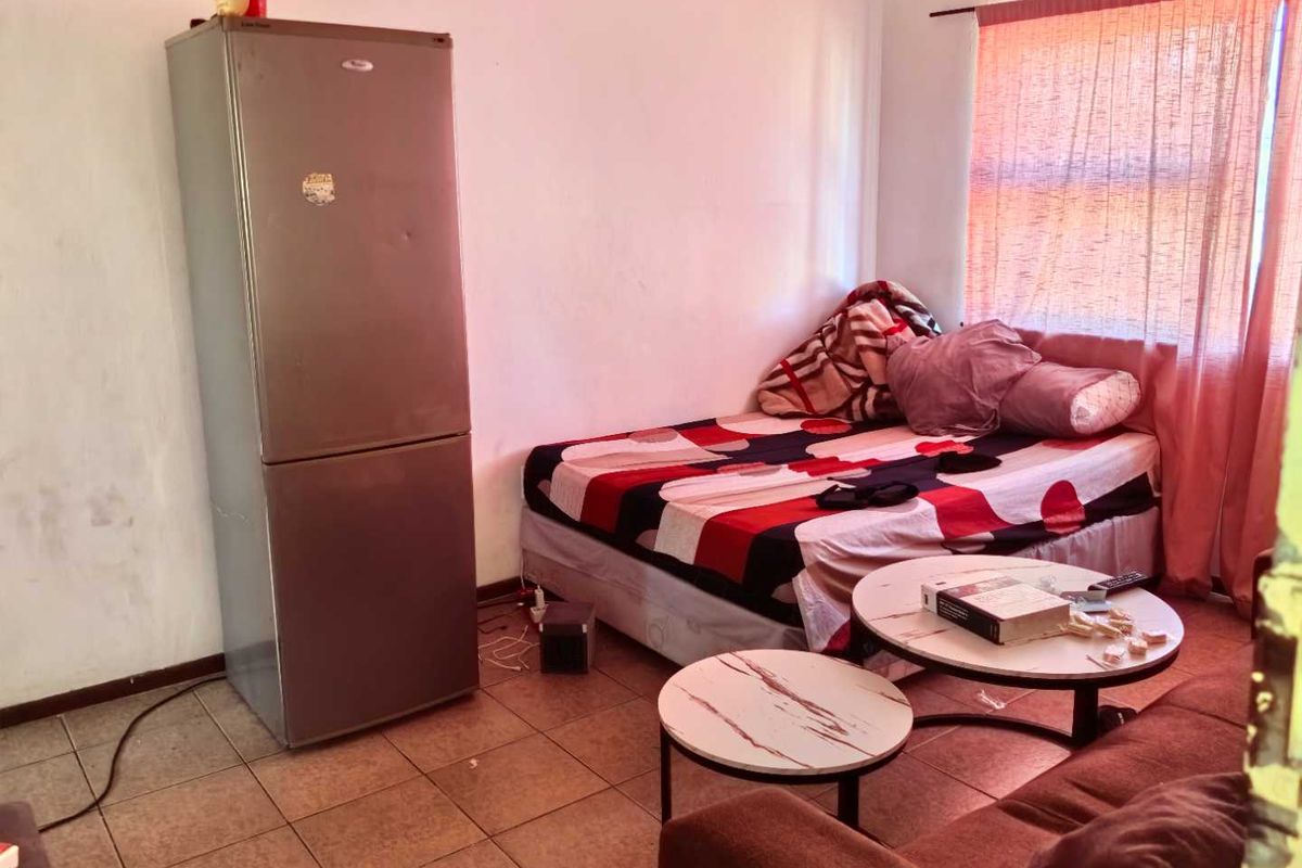 A bedroom featuring tiled flooring and a window with a curtain rod, currently used as a multi-purpose living space.