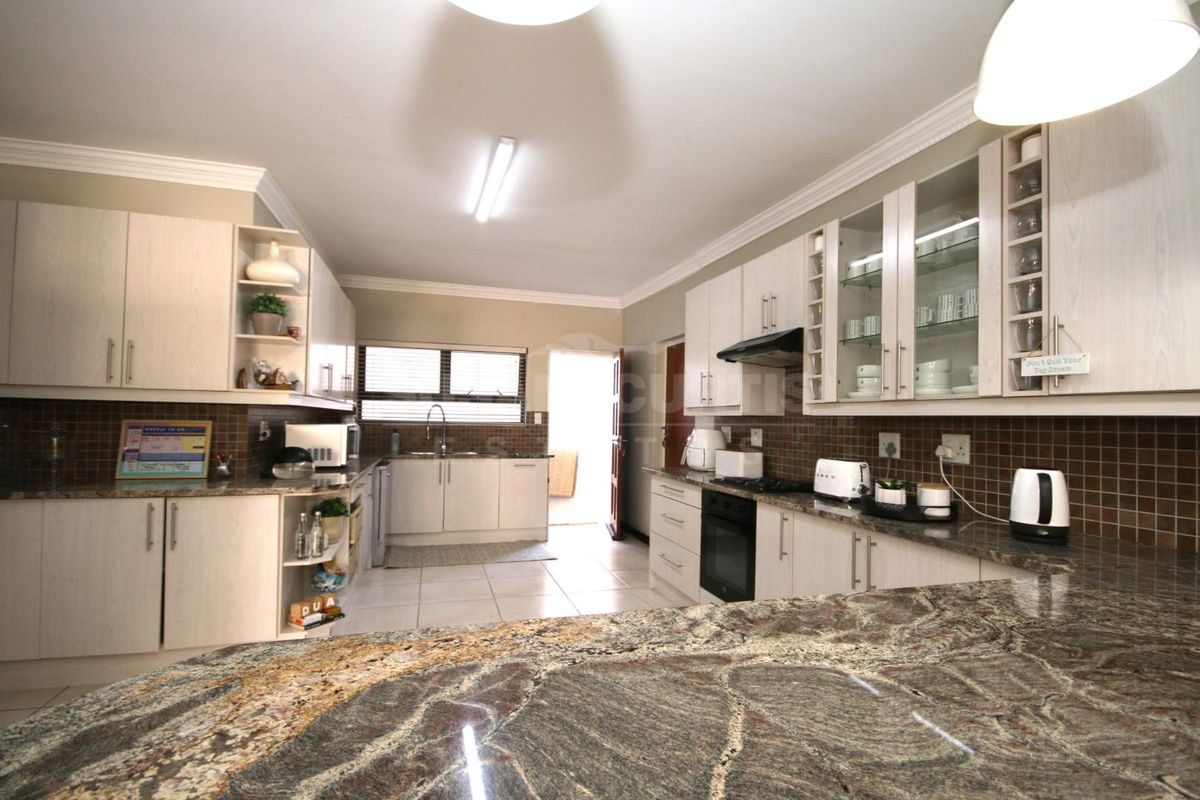 Spacious kitchen featuring granite countertops, extensive built-in cabinetry with glass-front displays, tiled backsplash, and integrated oven with extractor fan.