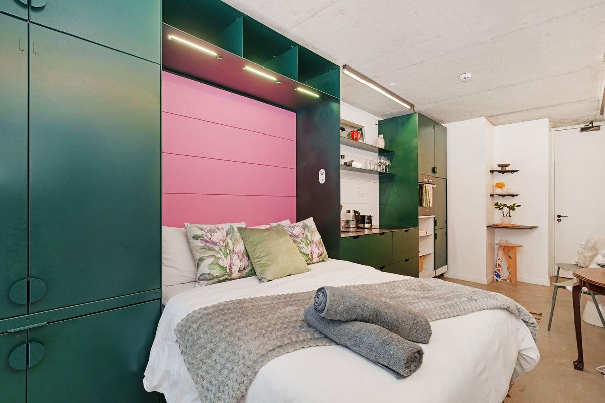 Modern studio bedroom featuring custom green built-in cabinetry, integrated shelving, and an exposed concrete ceiling with recessed lighting.
