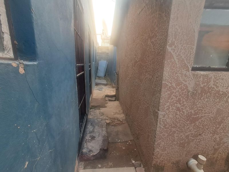 A narrow side passage between two exterior walls showing signs of wear, cracked plaster, and basic utility fixtures.