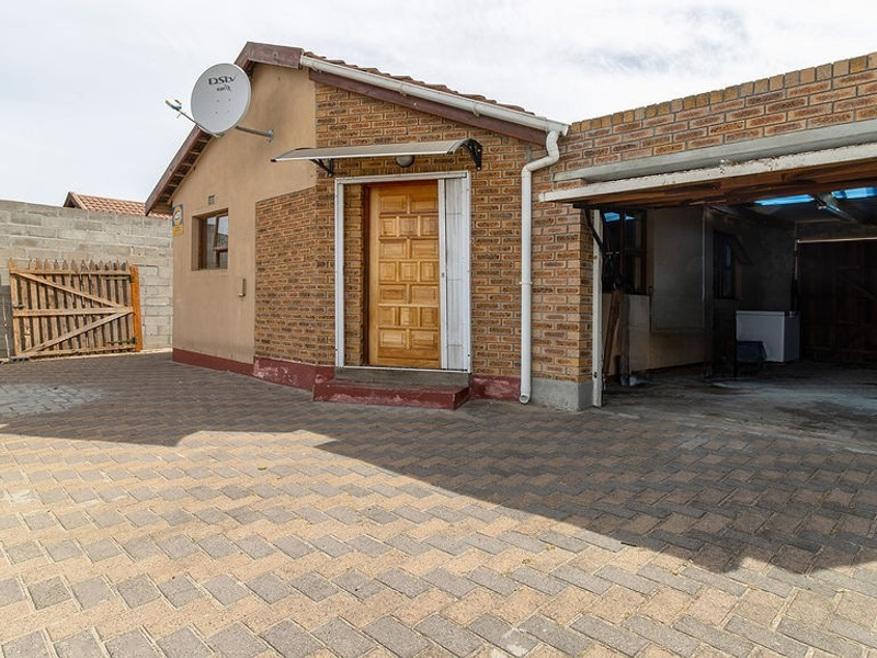 Front exterior view of a house featuring a paved driveway, brick facade, wooden entrance door, and an attached carport.