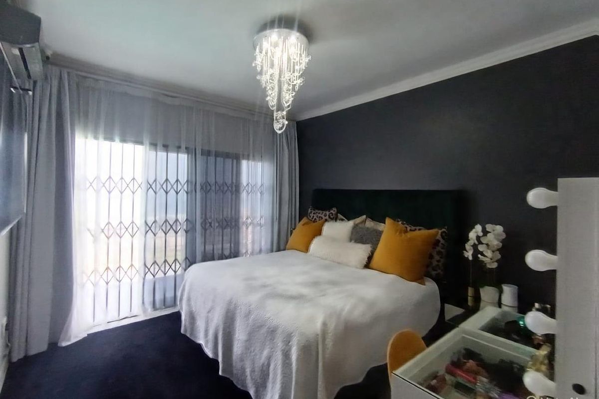 A well-maintained bedroom featuring a modern crystal chandelier, dark accent wall, and sliding glass doors with integrated security gate leading to the exterior.
