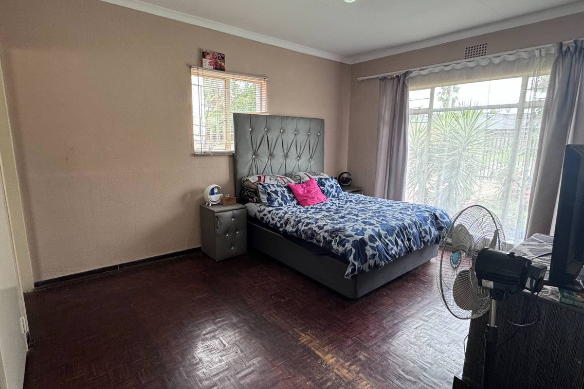 A spacious bedroom featuring original parquet flooring, large windows allowing natural light, and neutral wall finishes.