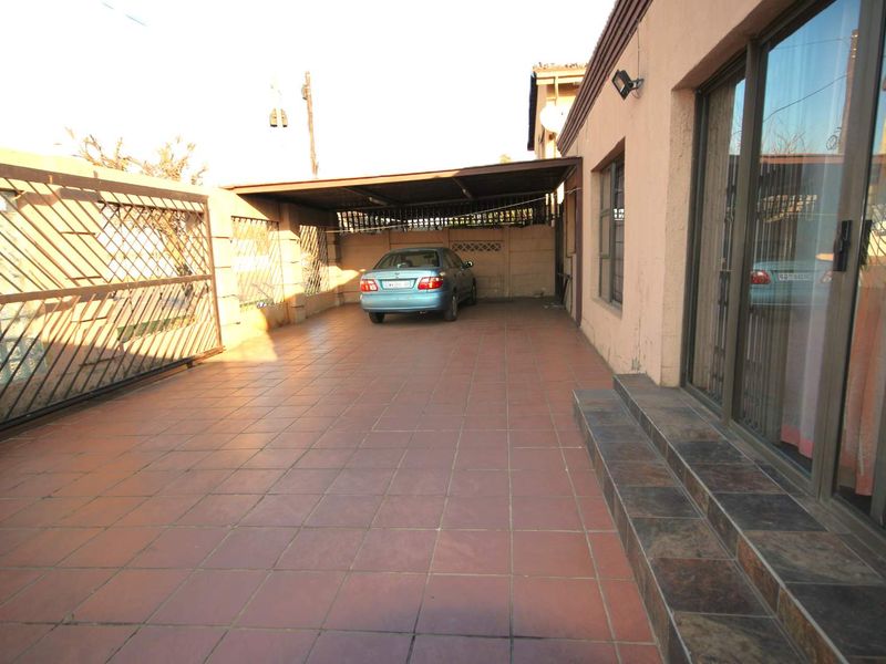 A paved outdoor carport area featuring a covered parking space, tiled flooring, and direct access to the home through sliding glass doors.