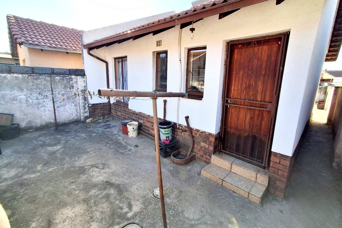 Rear exterior view of the property featuring a concrete patio area, brick and plaster facade, and a secure wooden entrance door.