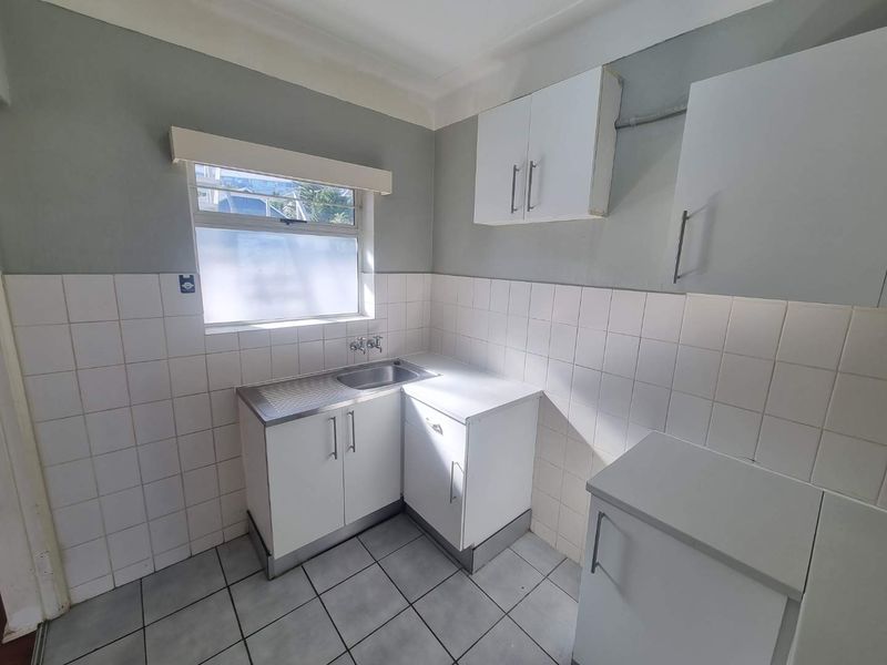 A compact, functional kitchen featuring white cabinetry, a stainless steel sink, tiled splashbacks, and tiled flooring, offering a clean and neutral space.