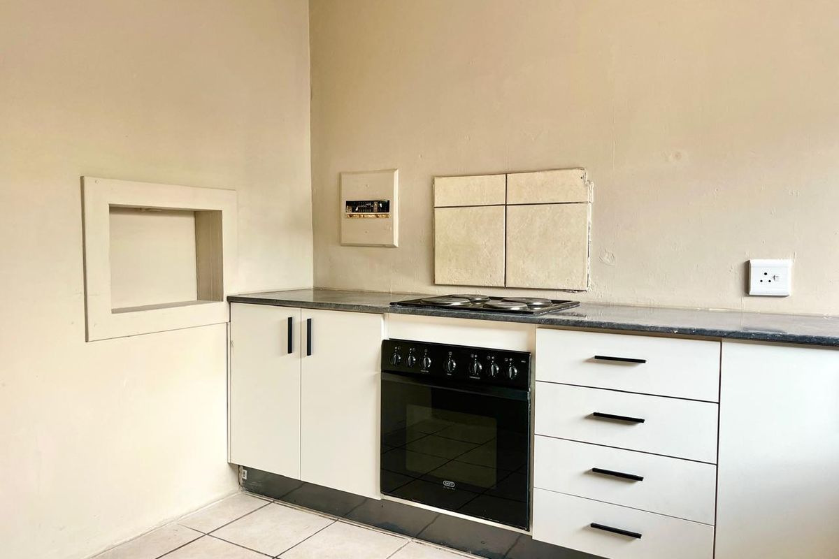 A compact kitchen featuring white cabinetry, a built-in oven with electric hob, and tiled flooring, ready for a modern update.