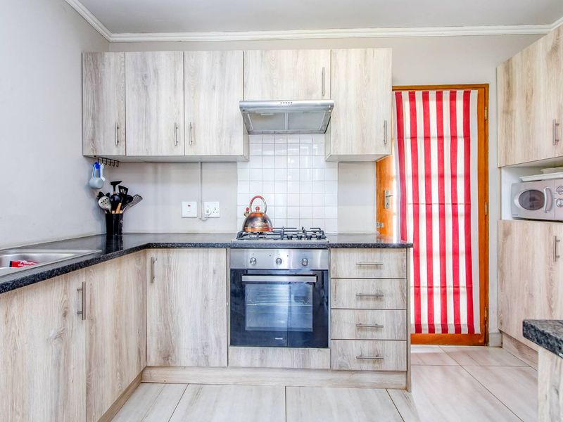 A functional kitchen featuring light wood-look laminate cabinetry, granite countertops, a gas hob with extractor, and a built-in oven with tiled backsplash.