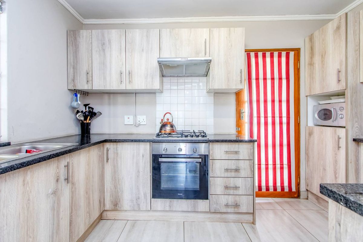 A functional kitchen featuring light wood-look laminate cabinetry, granite countertops, a gas hob with extractor, and a built-in oven with tiled backsplash.