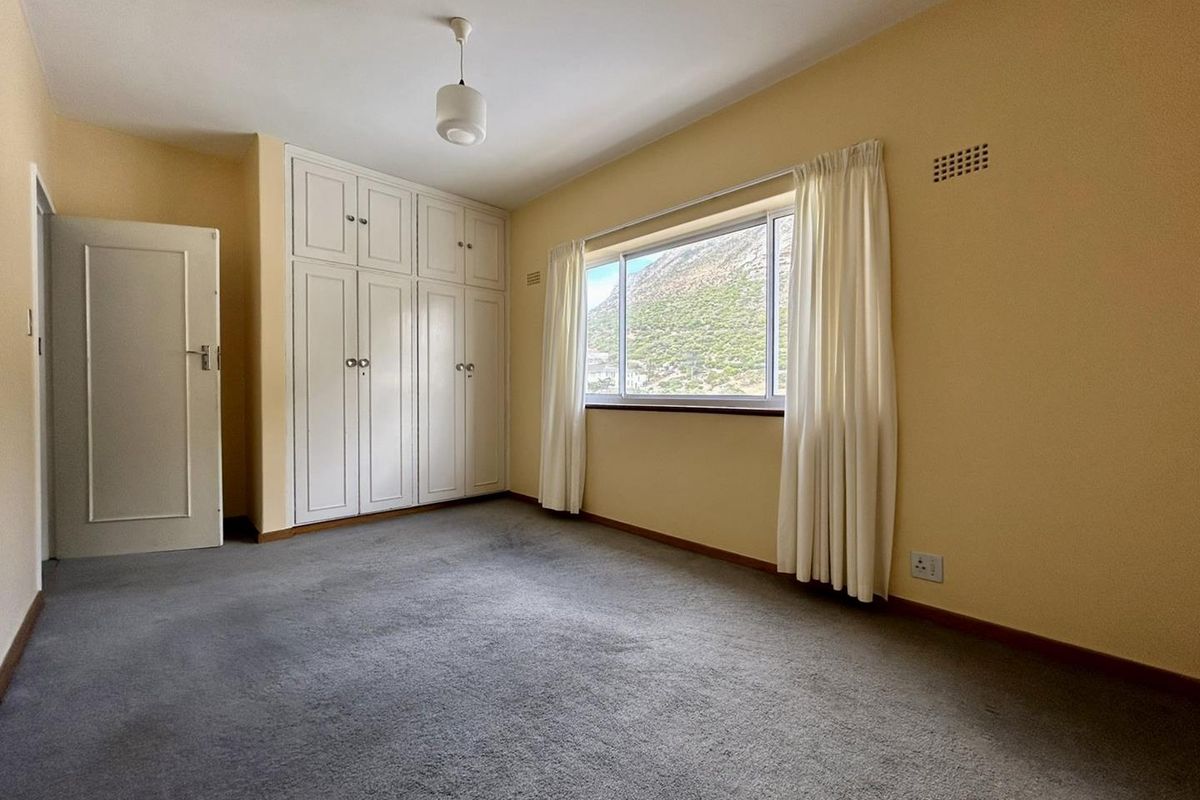 A spacious bedroom featuring built-in cupboards, neutral carpeting, and a large window offering natural light and mountain views.