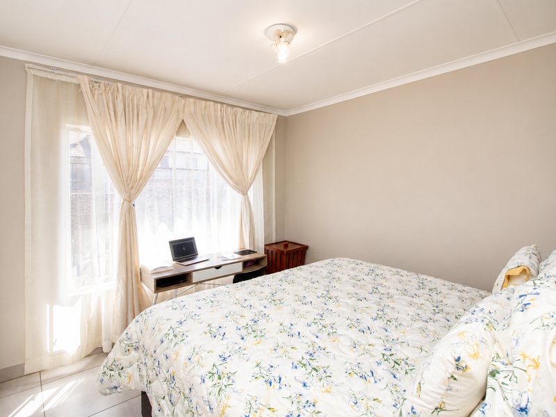 A well-lit bedroom featuring tiled flooring, built-in cupboard storage, and a window with curtain treatments, offering a functional and comfortable living space.