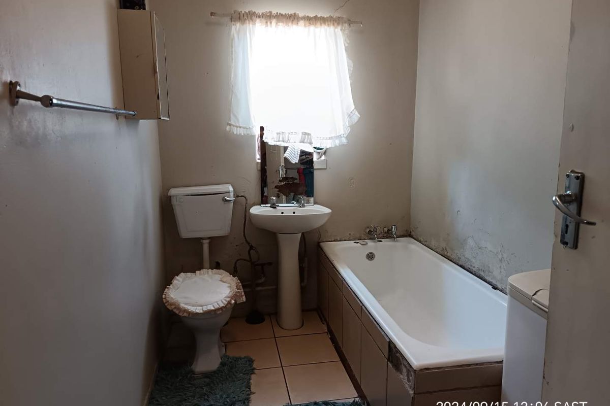 A dated bathroom featuring a standard bathtub, pedestal basin, and toilet, requiring significant renovation and cosmetic updates to improve its condition.