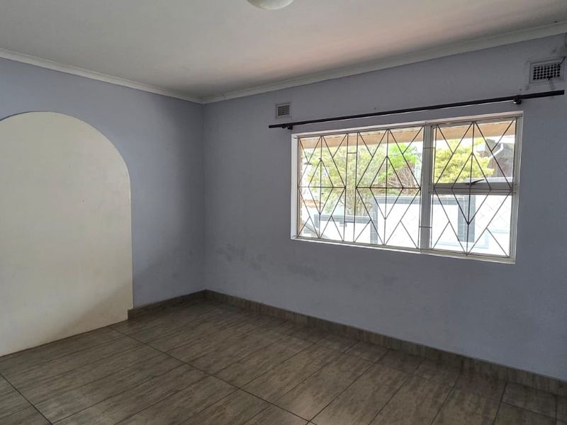 An empty bedroom featuring tiled flooring, an arched wall detail, and a window fitted with security burglar bars.