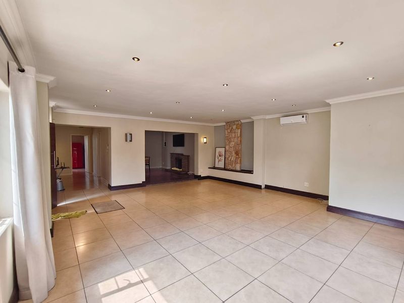 Spacious, open-plan living area featuring neutral tiled flooring, recessed lighting, a stone feature wall with a fireplace, and a wall-mounted air conditioning unit.