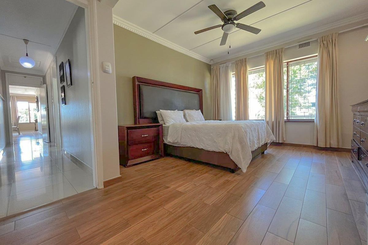 Spacious bedroom featuring wood-look flooring, a ceiling fan, and large windows with security bars, providing ample natural light.