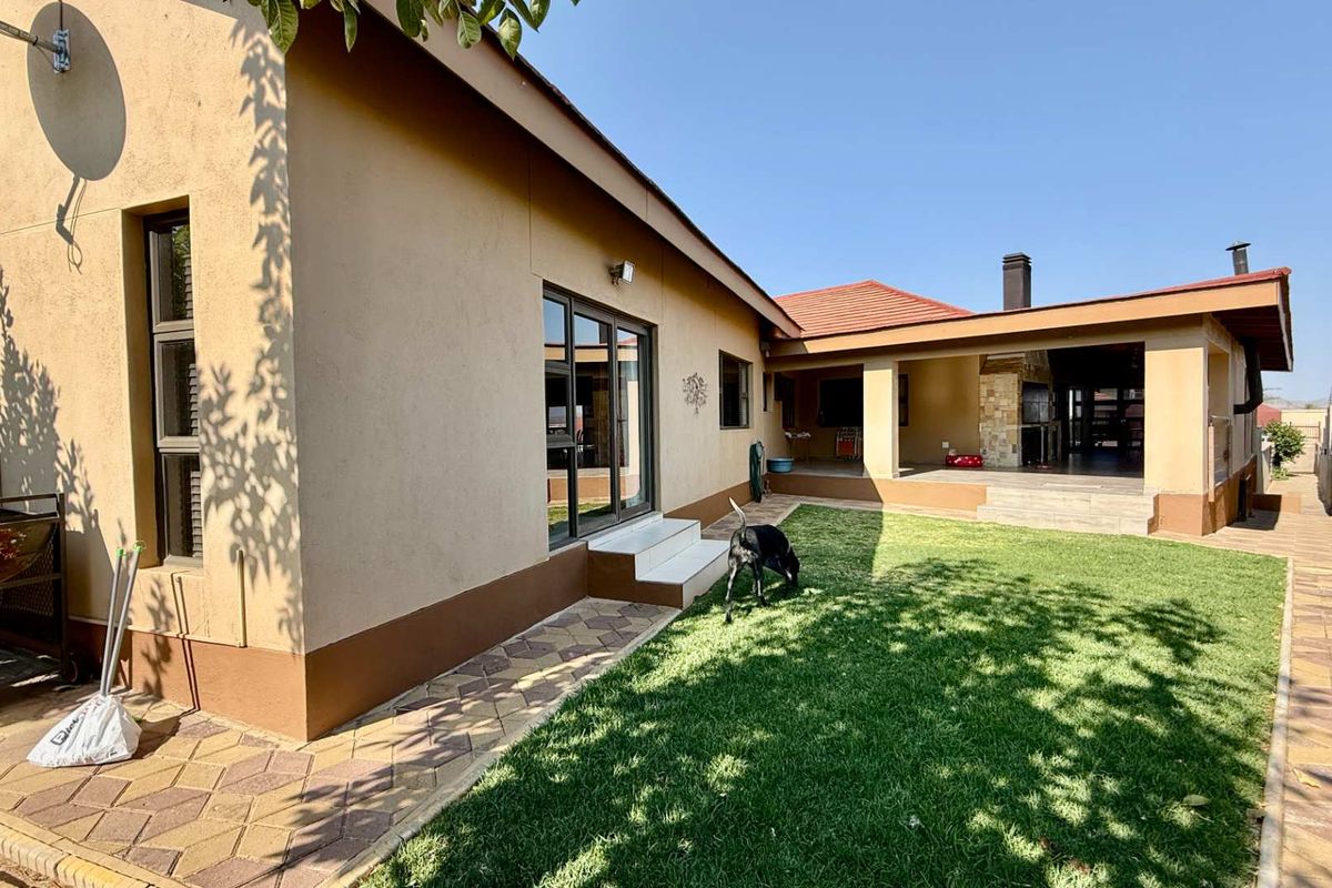 Rear view of the property featuring a covered patio with built-in braai, paved walkways, and a well-maintained lawn.