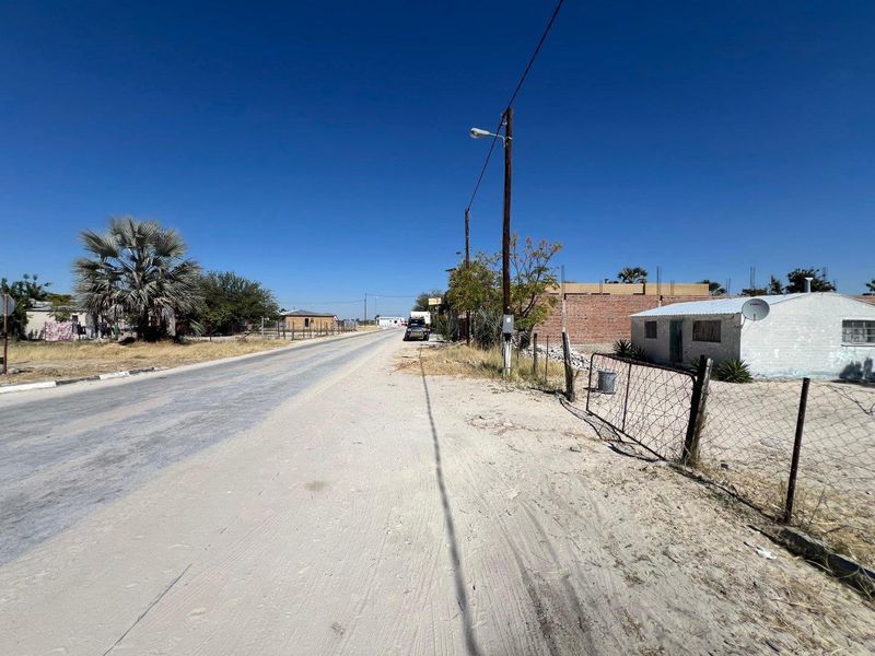 A street-level view showing the unpaved road, utility infrastructure, and surrounding residential properties in the neighborhood.